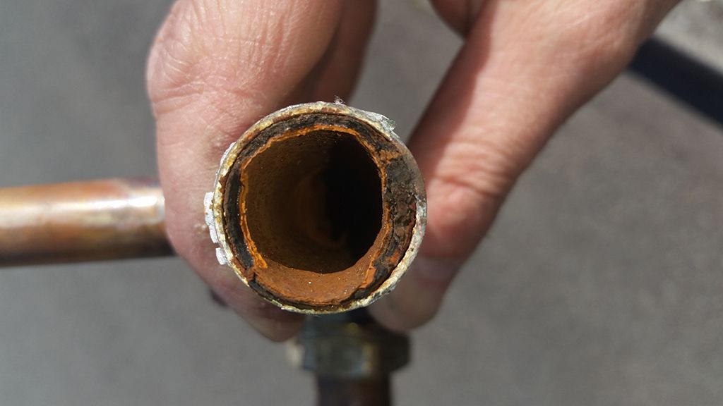 Photo showing a pipe that is corroded and clogged which may be prevented by power flushing the system